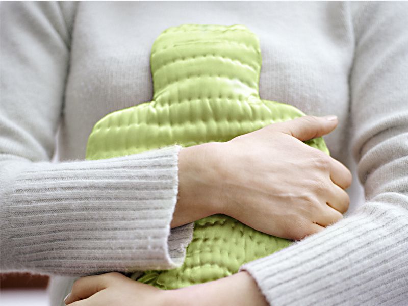 Frau hält Wärmflasche an den Bauch, um Menstruationsbeschwerden zu lindern
