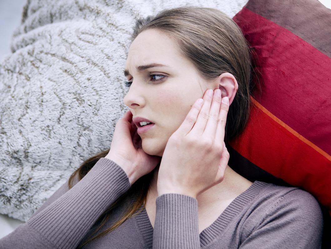 Frau liegt auf dem Sofa und hält sich schmerzerfüllt die Ohren